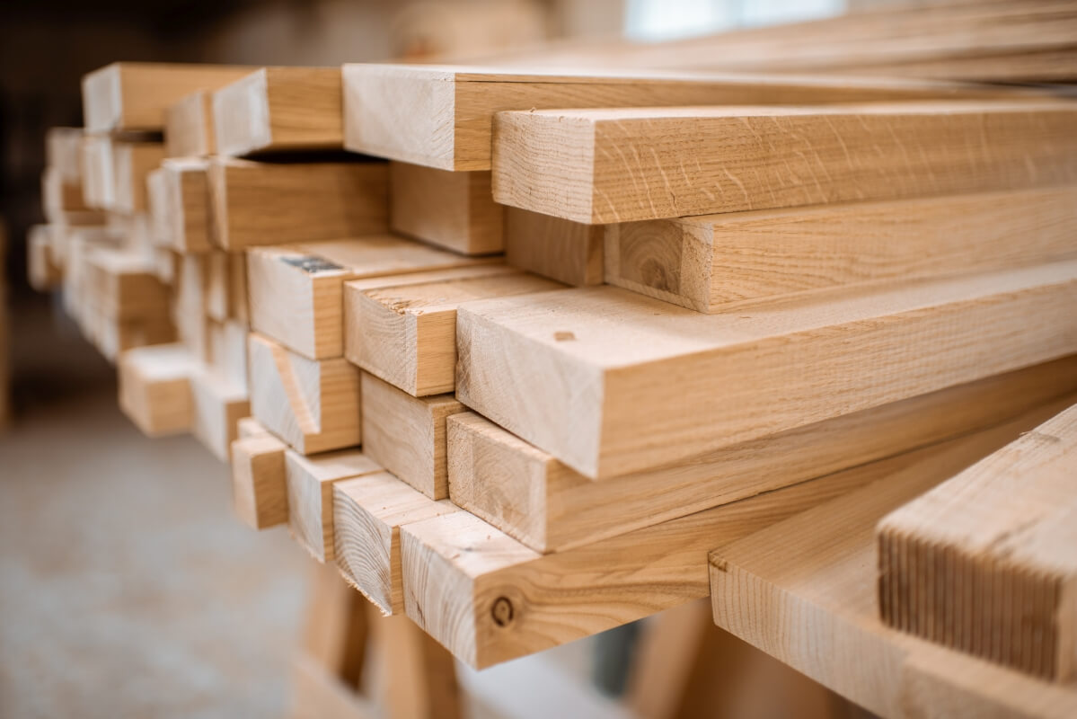 Stos kantówek ułożonych na stole stolarskim.